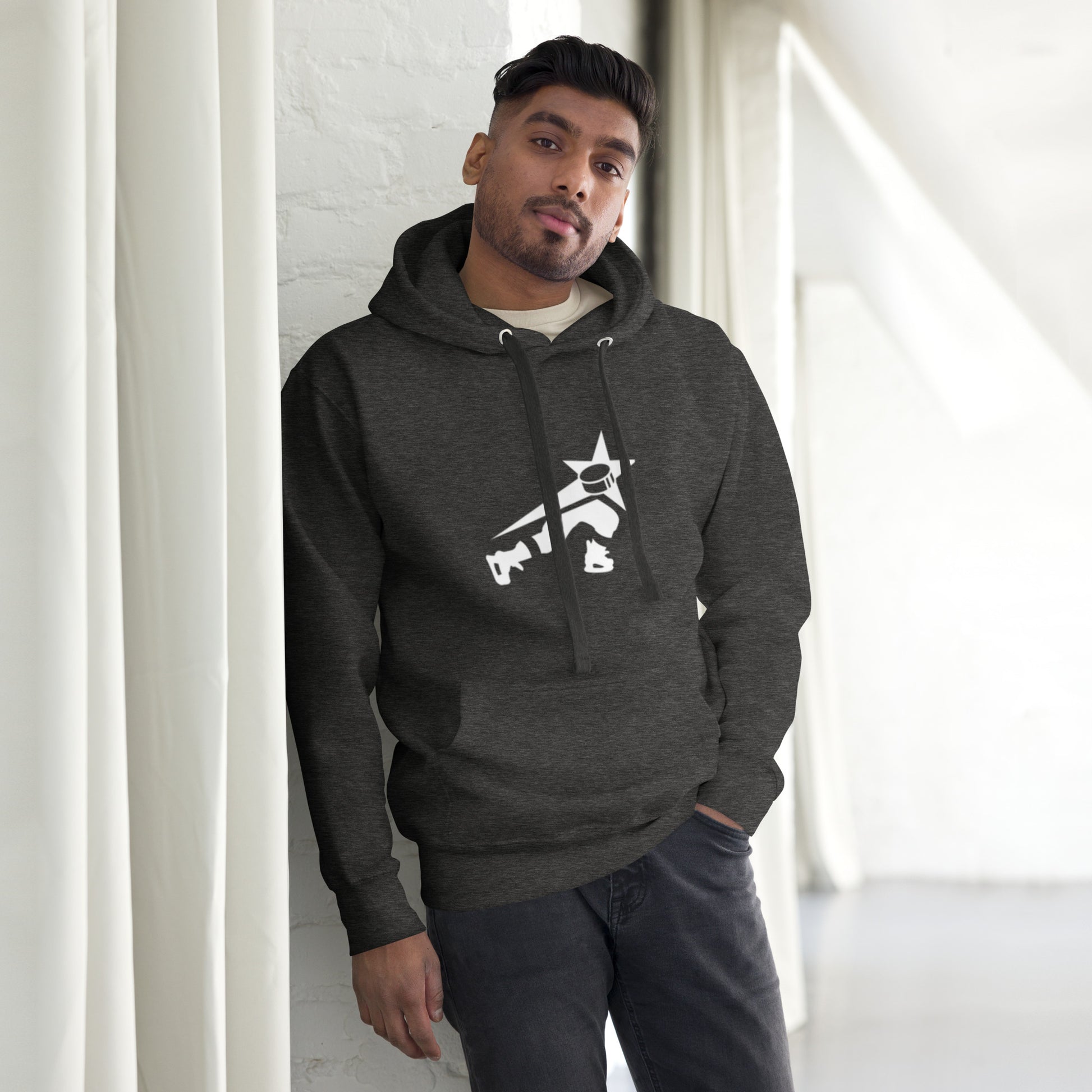 Confident man wearing a dark heather gray hoodie with a white stylized character graphic, leaning against a white brick wall.